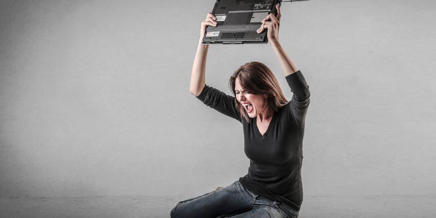 A frustrated woman holds her laptop computer above her head