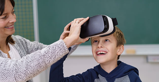 A young boy smiles as his teacher helps him put on a VR headset
